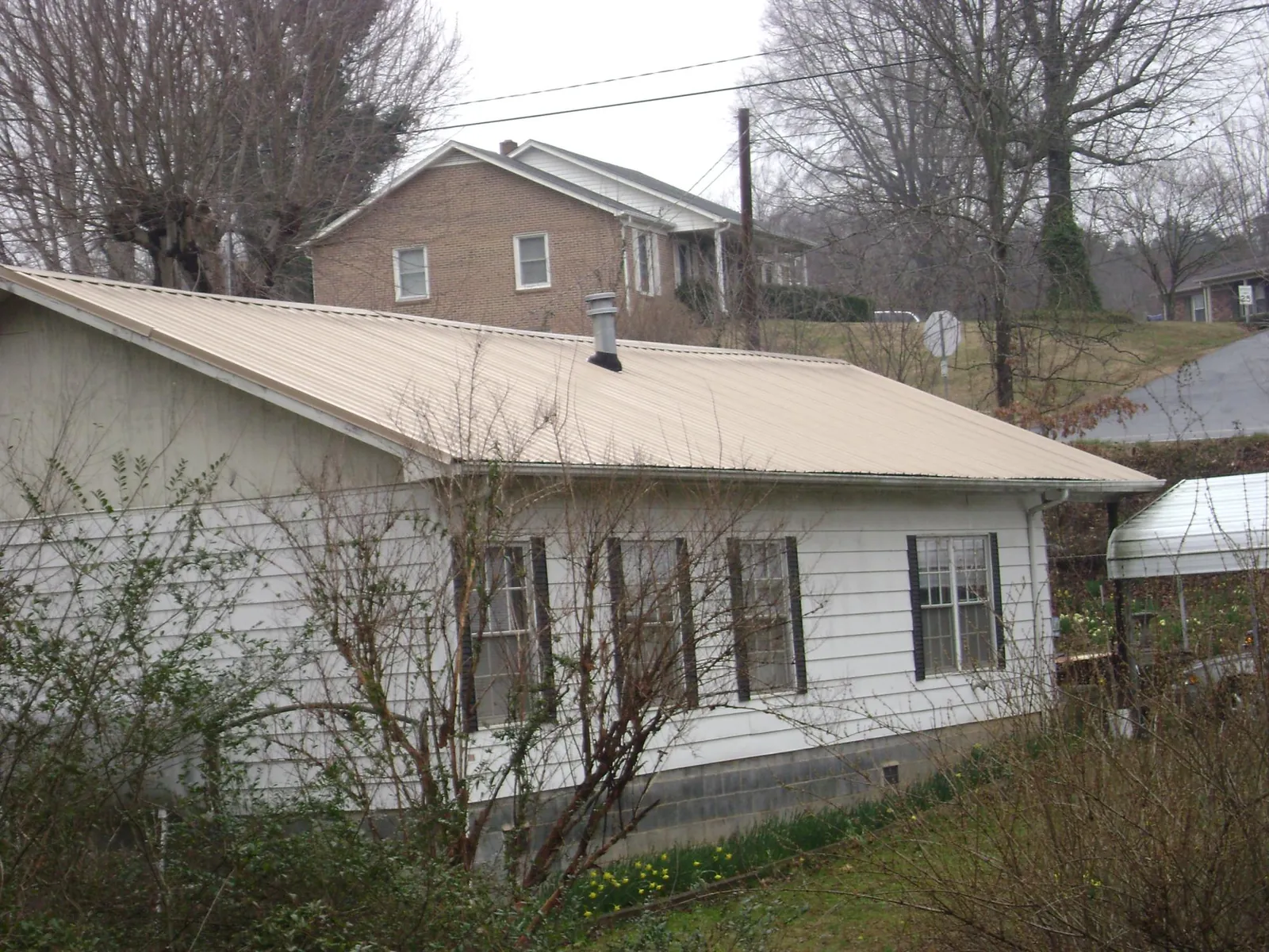 Tan metal roof on a white sided house set into a hillside — Commercial Roofing by Roofing Brothers in York